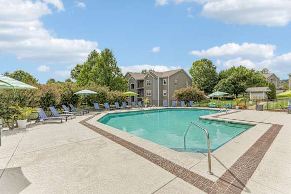 A swimming pool surrounded by a concrete patio and lawn chairs.