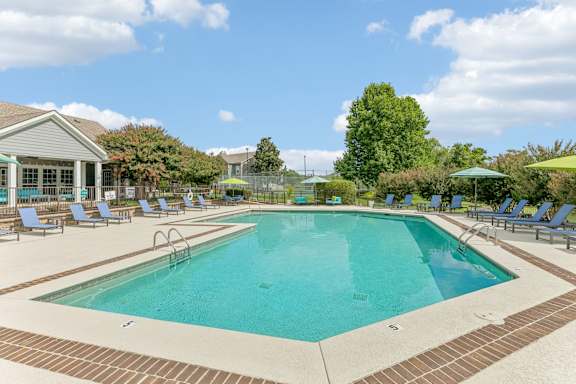 A large swimming pool surrounded by a brick border and lounge chairs.