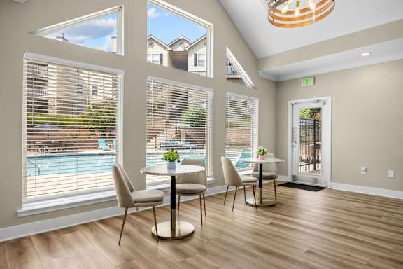 A dining room with a table and chairs and a view of a pool and houses outside the window.