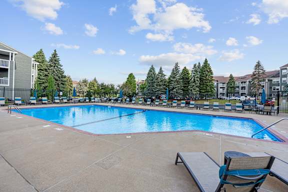 A large outdoor swimming pool surrounded by trees and chairs.