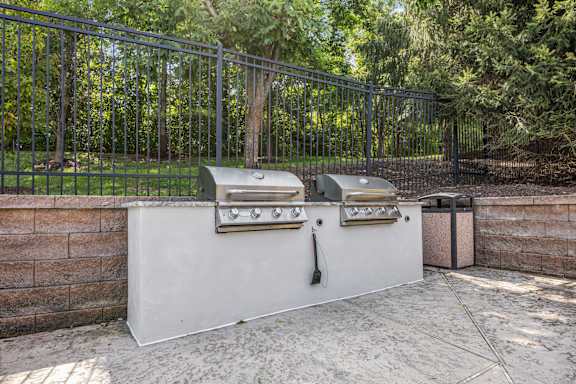 A barbecue grill with a sink and a trash can in front of a fence.