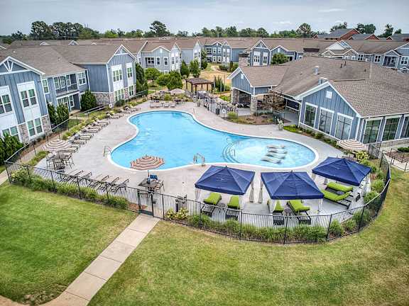A large swimming pool surrounded by a black fence and blue umbrellas.