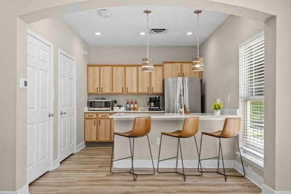 A kitchen with a refrigerator, microwave, and bar stools.