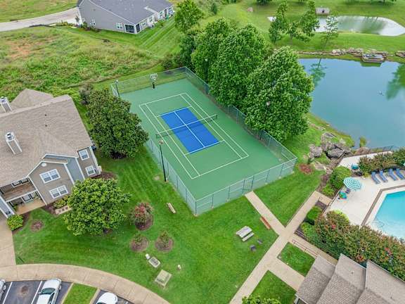 A tennis court is surrounded by a green fence and a pool.