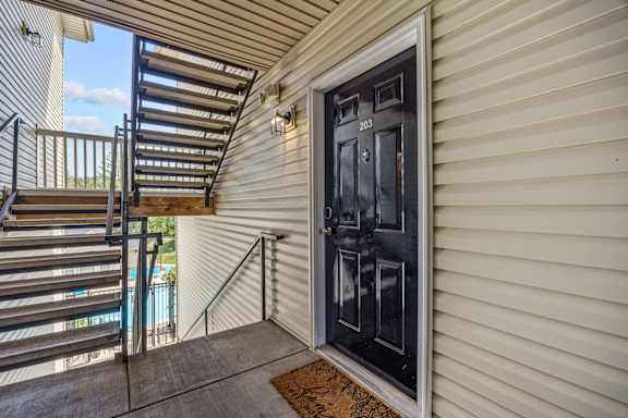 A black door with the number 203 on it is on a house with a beige siding.