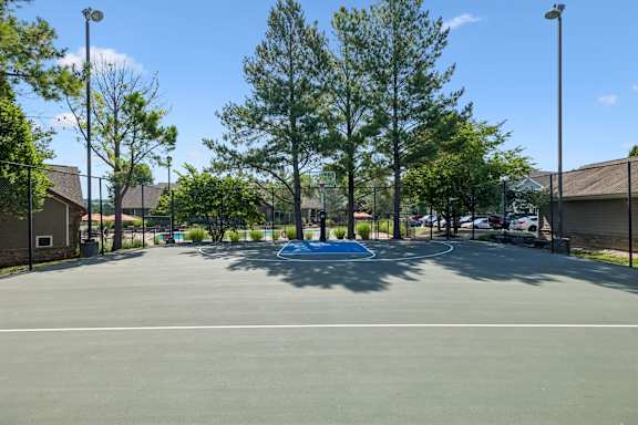 A basketball court surrounded by trees and a fence.