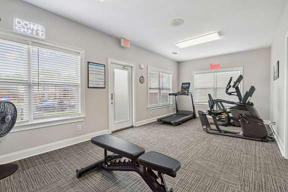 A gym room with a variety of equipment including treadmills, exercise bikes, and a bench.