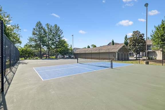A tennis court surrounded by a fence with a building in the background.
