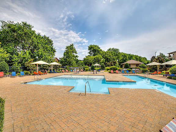 A large outdoor swimming pool surrounded by a brick patio and umbrellas.
