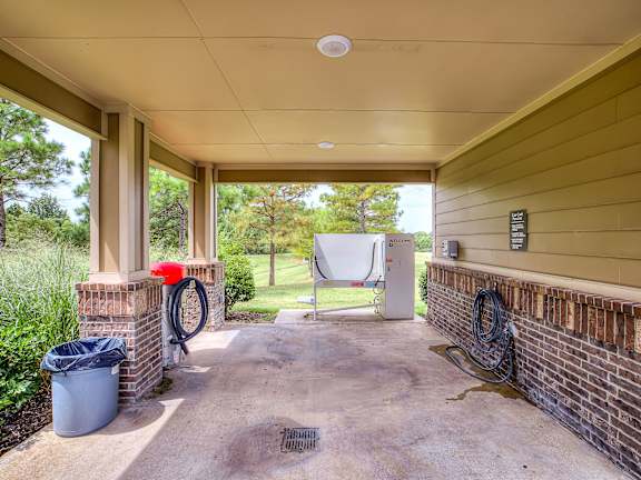A covered patio with a hose reel and a trash can.
