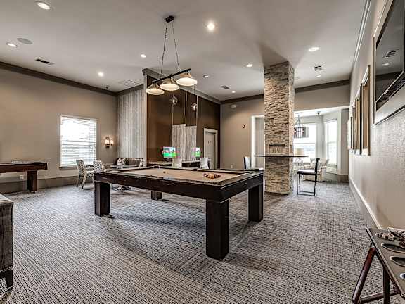 A billiard table is in the middle of a room with a stone pillar and a window.