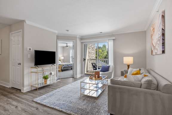 A living room with a grey couch, a TV on a stand, and a glass coffee table.