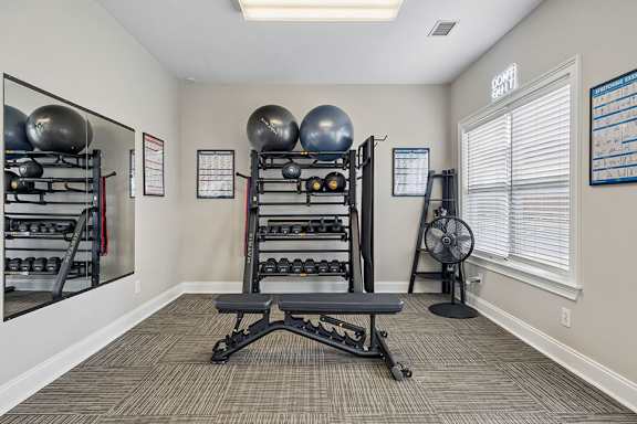 A gym room with a bench, weights, and a fan.