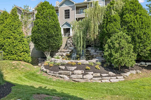 A well-manicured garden with a waterfall and a house in the background.