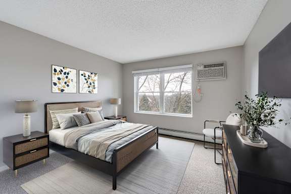 A spacious bedroom with a large bed, a nightstand, and a wooded view.