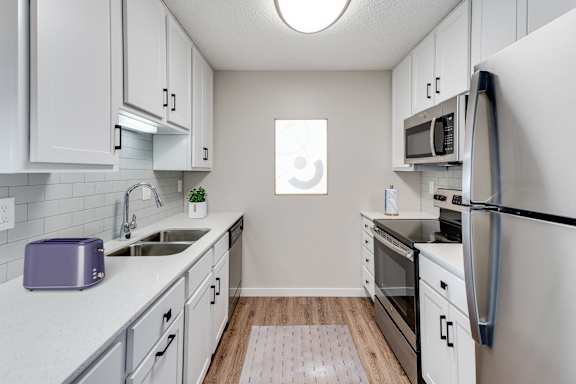 A kitchen with white cabinets, stainless steel appliances, and white counter tops