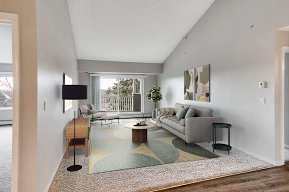 A living room with a couch, a coffee table, a vaulted ceiling, and access to a balcony.