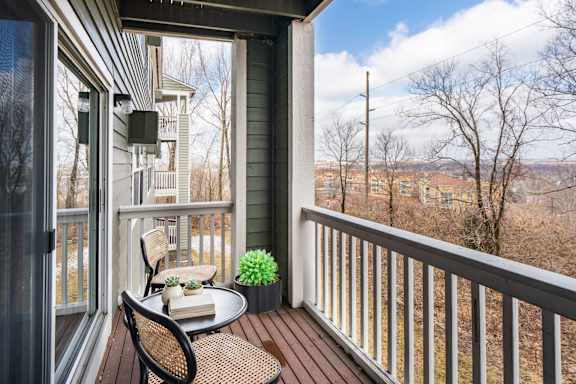 A large balcony with a chair and table with a view of the trees and town below.