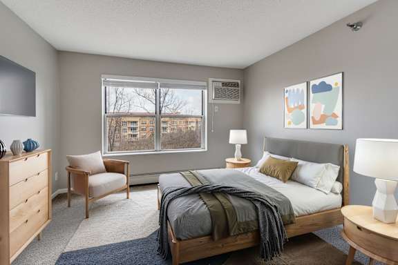 A bedroom with a bed, nightstand, chair, and window with trees outside.