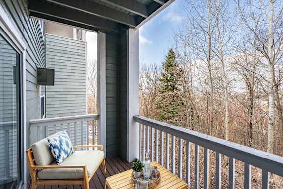 A wooden chair on a balcony with wooden railings and a wooded view beyond.
