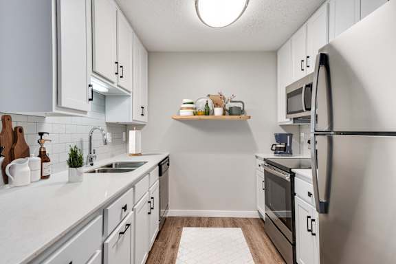 A kitchen with white cabinets and black knobs, stainless steel appliances, and wood-like flooring.