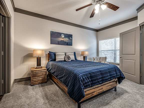 A bedroom with a bed, two lamps, and a ceiling fan.
