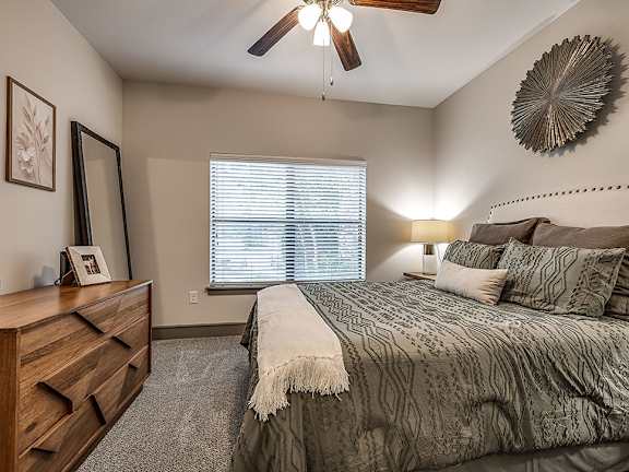 A bedroom with a bed, dresser, and window with blinds.