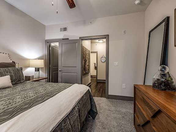 A bedroom with a bed, dresser, mirror, and a ceiling fan.