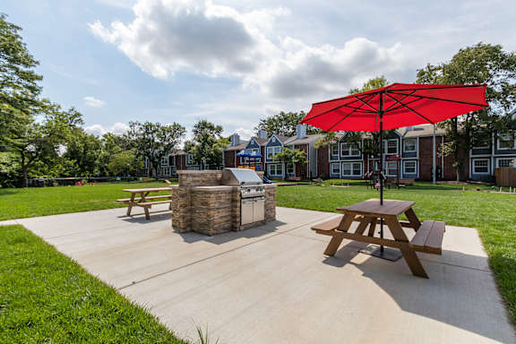 A picnic table with a red umbrella is in the middle of a concrete area.