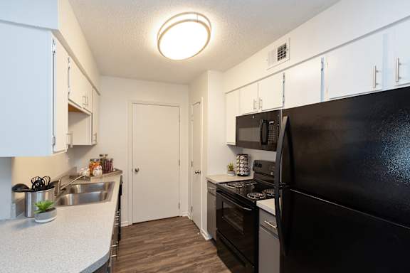 A black refrigerator sits in a kitchen with white cabinets and a white countertop.