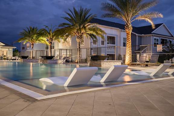 Zero-Entry Pool Lit Up At Night With Sun Lounger Chairs