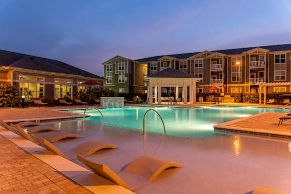 Resort-Style Pool Lit Up At Night With Water Lounge Chairs