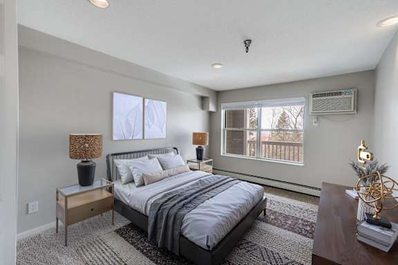 A bedroom with a large bed and a window overlooking a balcony and a wooded view.