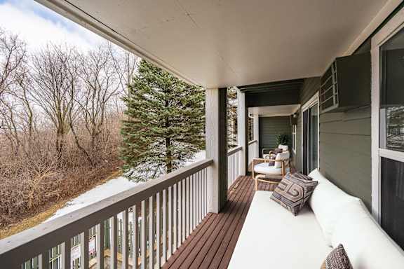 A balcony with an outdoor white couch and a brown pillow.