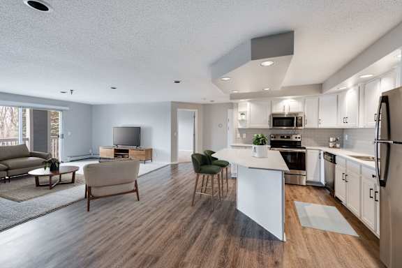 A modern kitchen with a white island, stainless steel appliances, and wood-like floors.