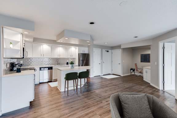 A large, modern kitchen with white cabinets and a wooden floor with a desk nook in the background.