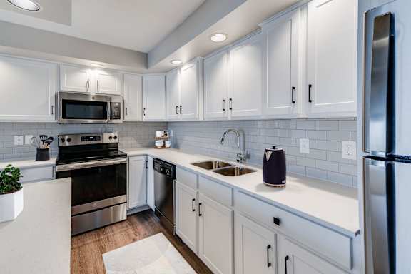 A modern kitchen with many white cabinets, a white backsplash, and stainless steel appliances.