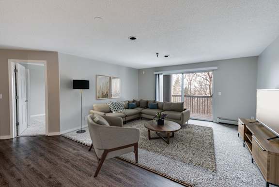 A carpeted living room with a sliding glass door leading to a balcony.