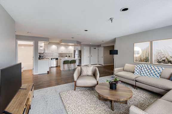 A modern living room with a kitchen in the background, featuring a television, two chairs, a coffee table, and a couch.