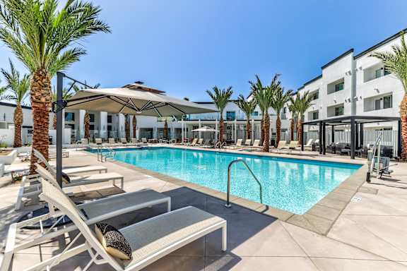 A pool surrounded by palm trees and lounge chairs.