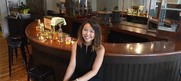 A woman in a black dress sits at a bar.