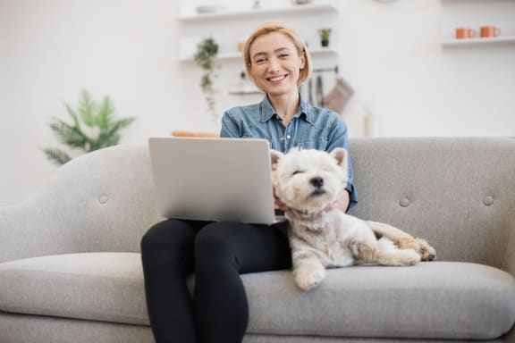 a woman sitting on a couch with a dog and using a laptop