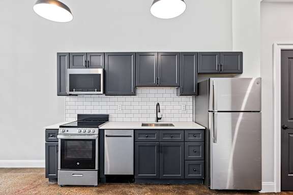 A kitchen with black cabinets and a stainless steel refrigerator.