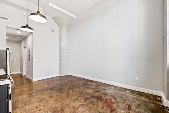 A room with a dirty floor and a kitchen area in the background.