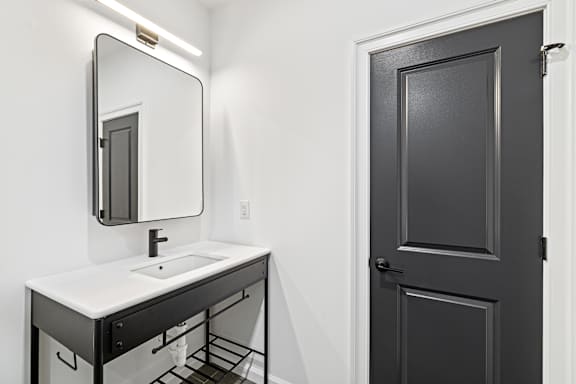 A bathroom with a sink, mirror and door.