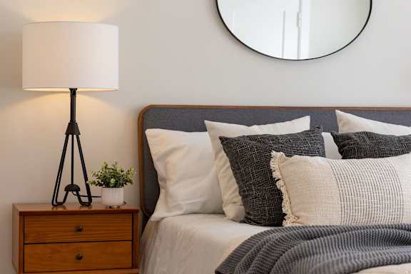 A bedroom with a bed, pillows, a lamp, and a mirror. at Anderson Center Apartments, Mullins