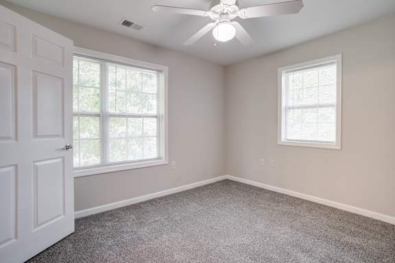 A room with a ceiling fan and two windows.