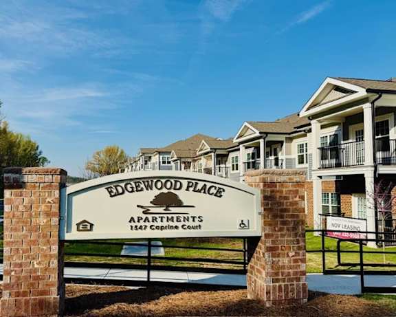 A sign for Edgewood Place Apartments stands in front of a row of houses.