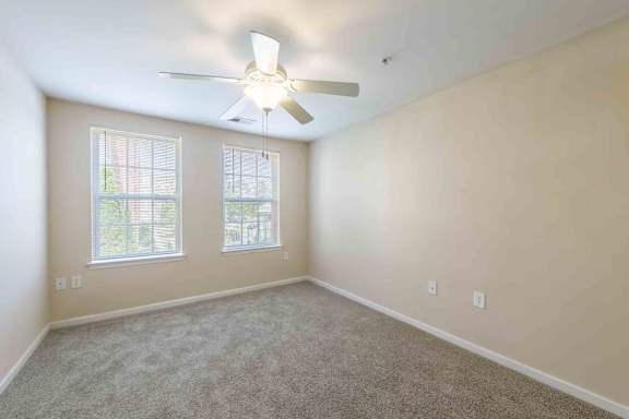 A room with a ceiling fan and two windows at Granite Falls Apartments, Rolesville
