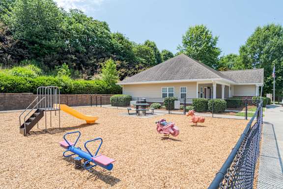 A playground with a slide, swings, and a seesaw in front of a house at Greylin Ridge Apartments, North Carolina